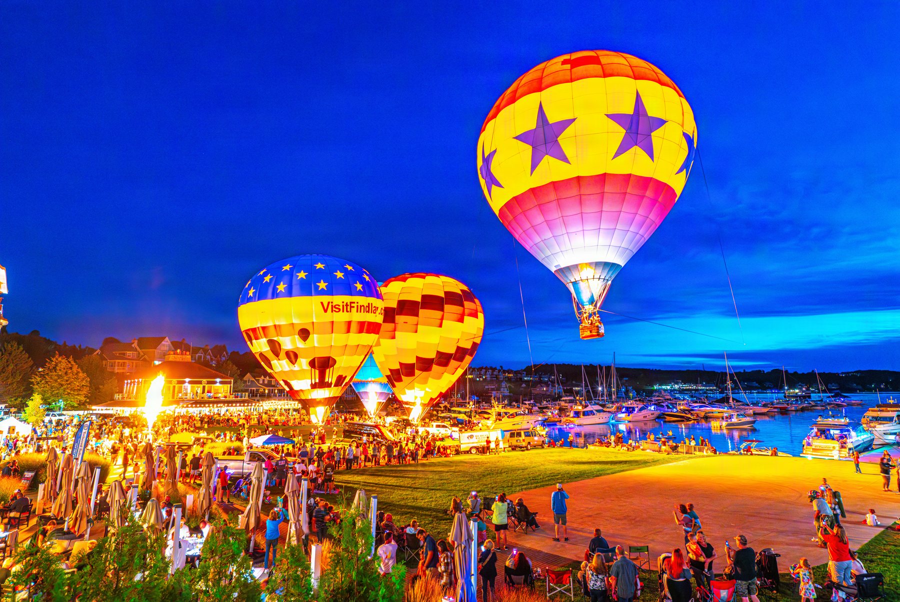 Hot air balloons glowing at dusk over the crowd and marina at Bay Harbor during the night glow
