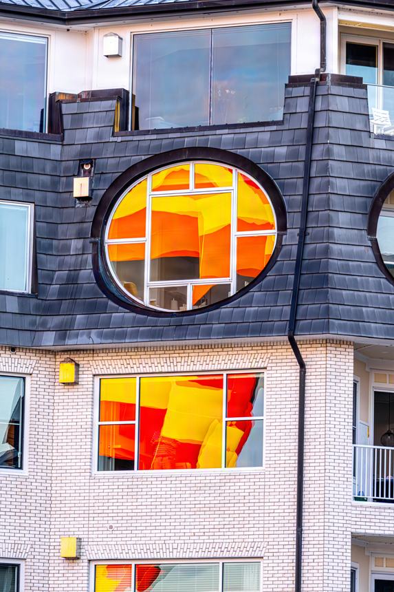 A round dormer window on a Bay Harbor building filled with the orange and yellow reflection of a passing hot air balloon