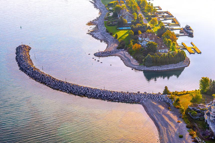 Aerial of a curving stone breakwater enclosing turquoise shallows beside a small wooded point