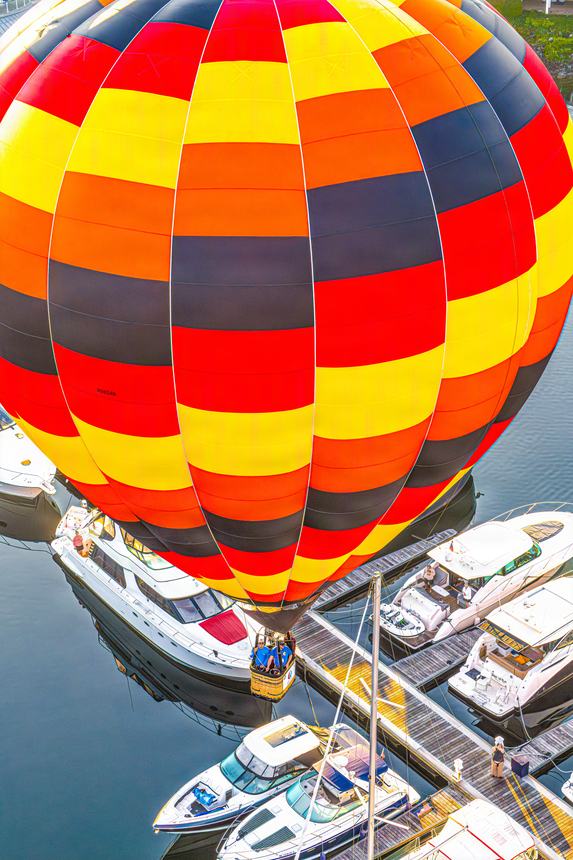 A red, yellow and black striped balloon descending directly over the marina docks and moored yachts