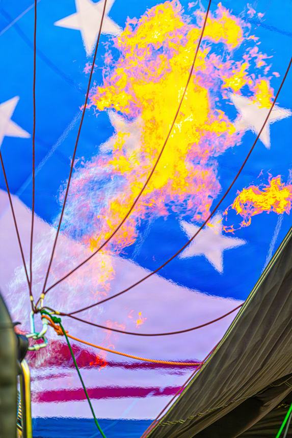Looking up inside a star-spangled balloon envelope as the burner flame curls against the fabric