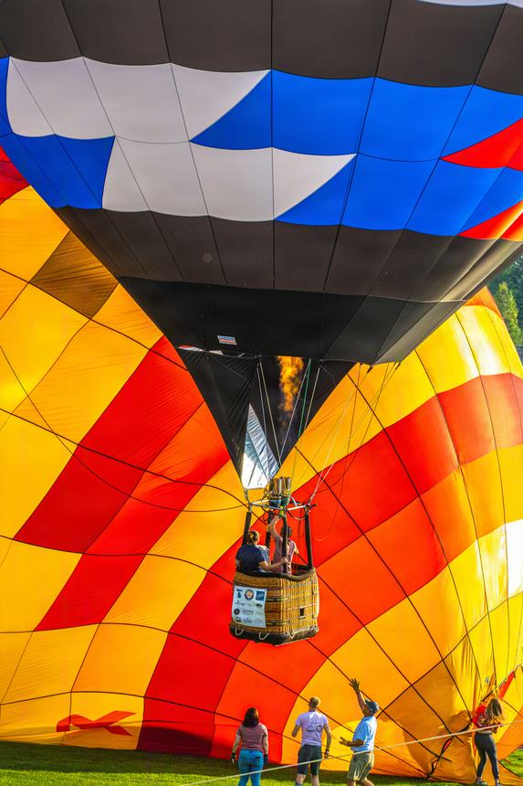 A red, orange and yellow balloon envelope filling on the grass while a second balloon stands inflated behind it and ground crew hold the crown lines
