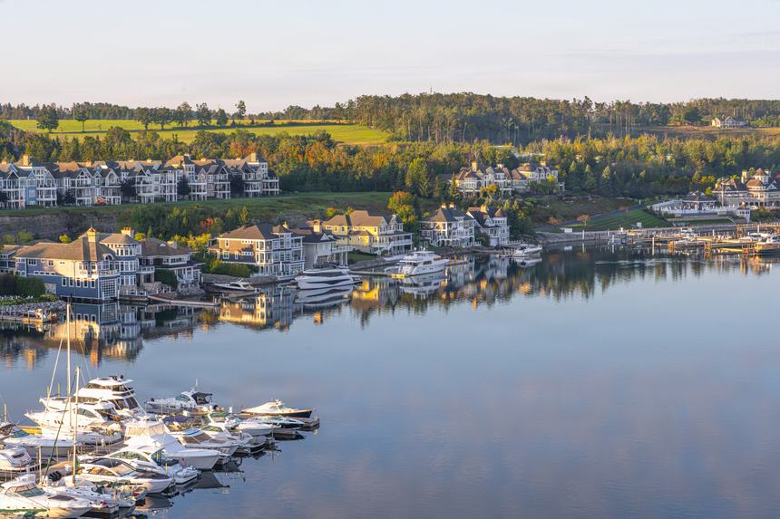 Aerial of the Bay Harbor marina basin at dawn, sailboats and yachts on mirror-calm water with homes and green slopes beyond