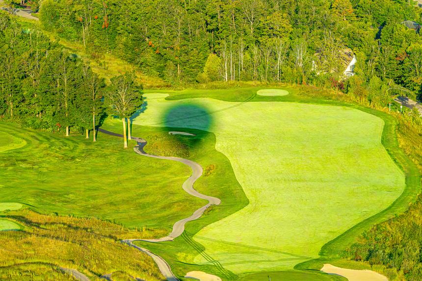 Aerial of a golf course fairway and green with the soft round shadow of a hot air balloon falling across the grass