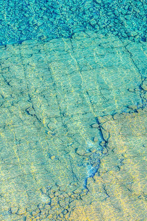 Abstract aerial of clear turquoise shallows over pale limestone shoals, the rock fractured into a fine grid of seams