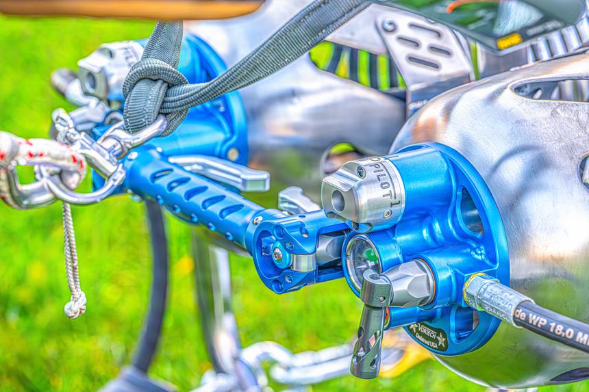 Detail of a balloon's blue anodised burner block, blast valves and pilot light hardware above a green field