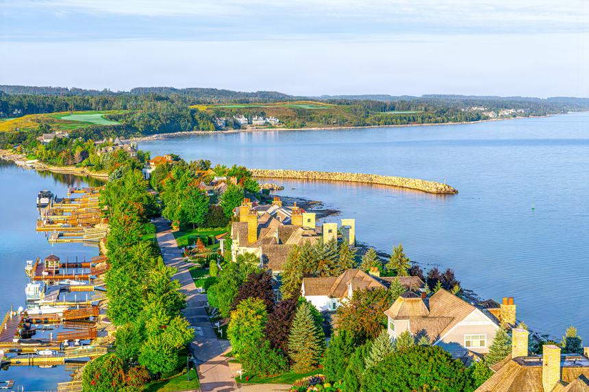 Aerial along the Bay Harbor peninsula showing the marina, waterfront homes and the stone breakwater reaching into Lake Michigan