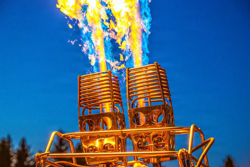 Close view of a balloon's twin burners firing a tall blue and yellow flame against a deep blue sky