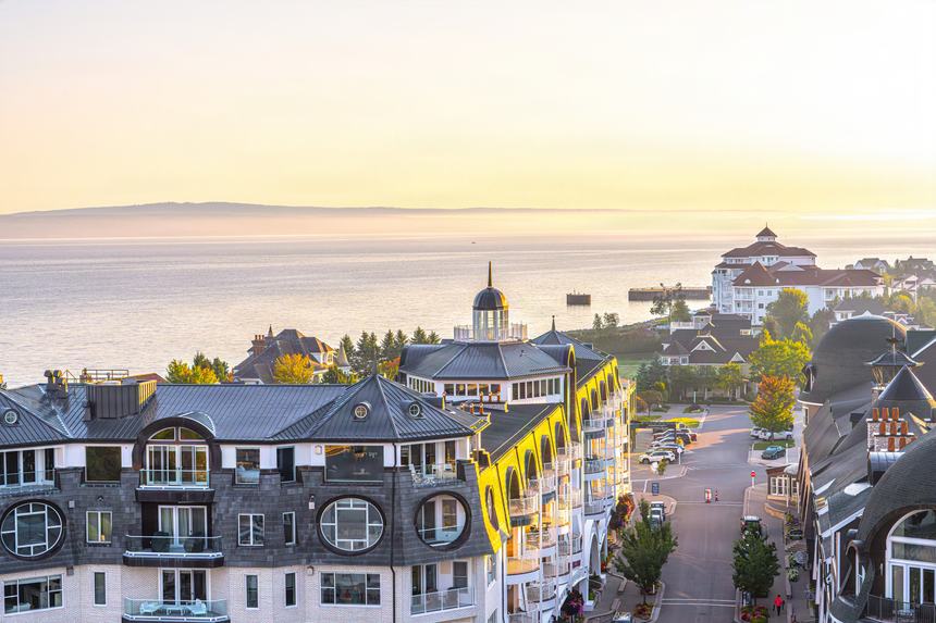 Aerial of the Village of Bay Harbor rooftops with Little Traverse Bay and the Inn beyond, under a pale gold dawn sky
