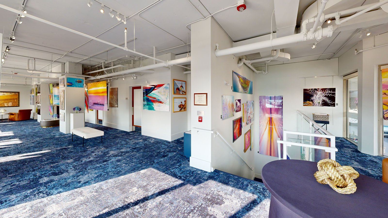 The main exhibition floor at Alexander Kippe Fine Art, Bay Harbor &mdash; aluminum works lining the walls above deep blue carpet